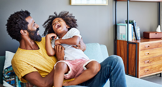 Father laying on bed tickling his young daughter who is laughing