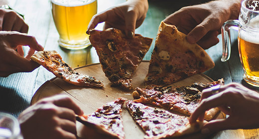 Friends sitting at a table and all reaching for a slice of pizza