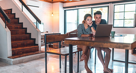 Young couple sitting at a kitchen table looking at a laptop computer