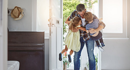 Father hugging his young son and daughter after walking in the door from a long day at work