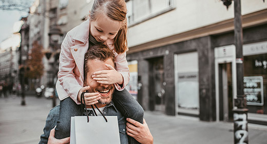 Little girl riding piggyback on her father while holding a shopping bag after leaving a store