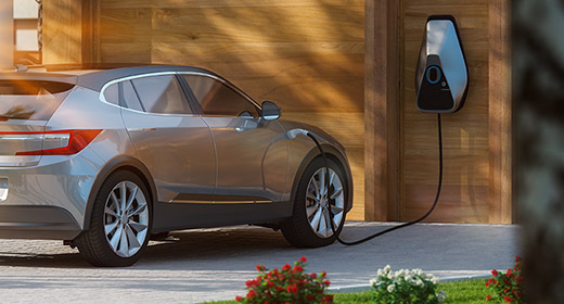 A high end electric car is being charged in front of a fancy house