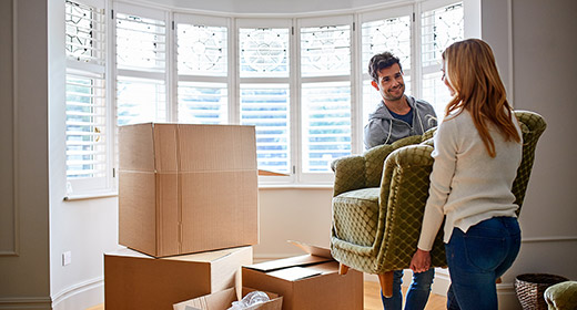 Man and woman couple carrying a couch into their new home sorrounded by moving boxes