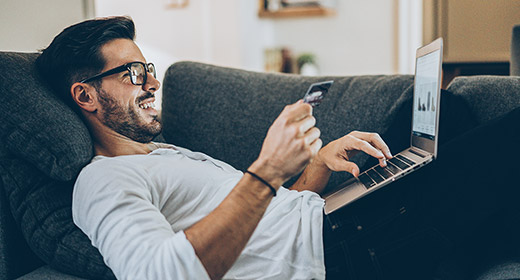 Man laying on his couch doing online shopping with his laptop and entering a credit card number