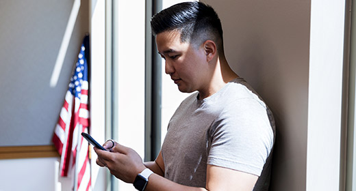 Man leaning against a wall while typing on his mobile phone