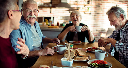 Group of older friends sitting at a kitchen table eating and laughing