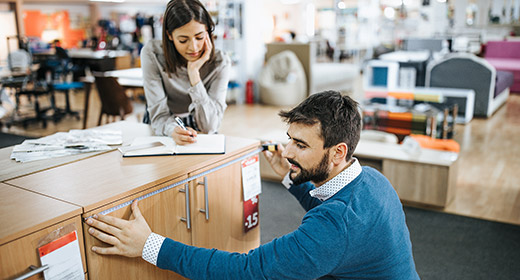 Man and woman looking at a dresser in a furniture store Man is measuring width while the woman writes down the results