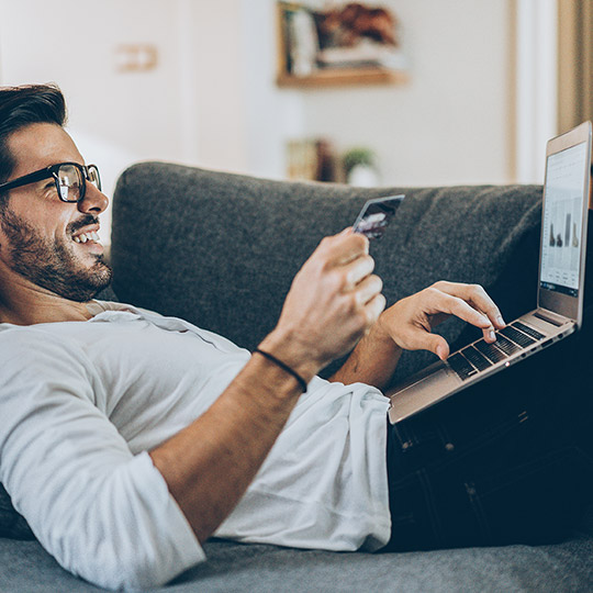 Man laying on his couch doing online shopping with his laptop and entering a credit card number