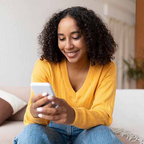/getmedia/109850d8 c537 4c7d b9ff 1a256ab347d3/woman sitting on her couch smiling at her phone 480x480