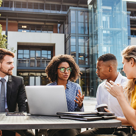 Coworkers sitting outside at a table and discussing a work project