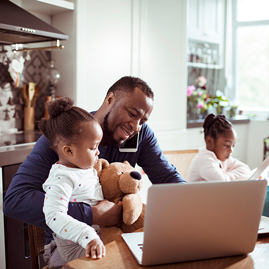 Father caring for his young daughters while on the phone at a kitchen island