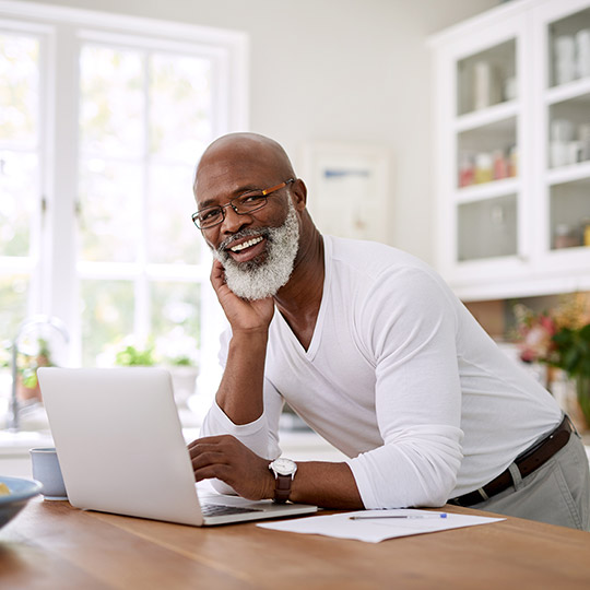 Older male leaning on a kitchen island in front of his laptop computer