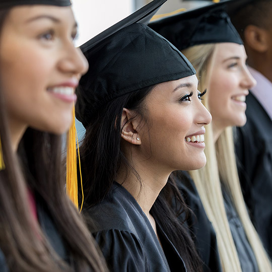 Soon to be college graduates standing in a row in their caps and gowns