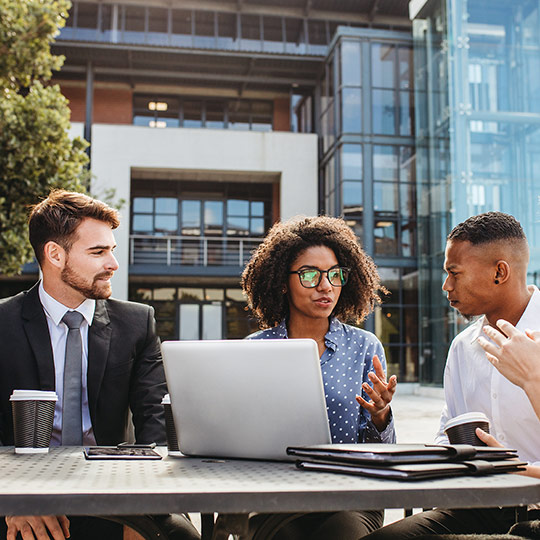 Group of coworkers sitting outside at a table and discussing their business