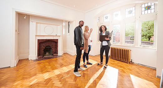 Realtor showing a couple a room in a home for sale room has a fireplace, hardwood floors, and a wall attached heating unit