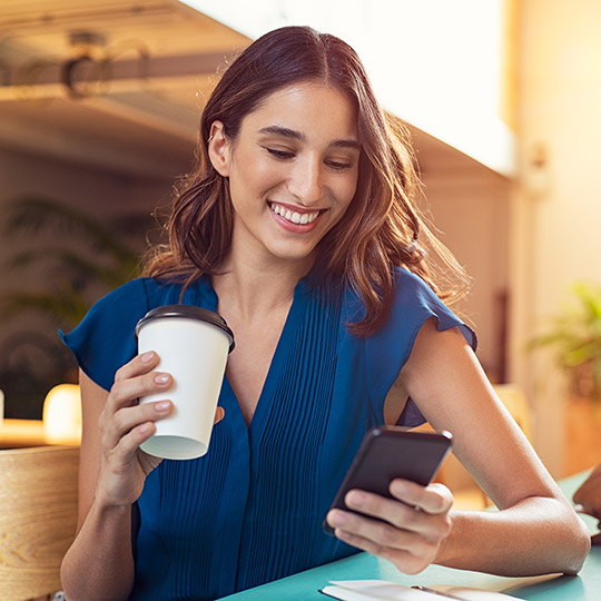 Woman at coffee shop looking at her phone while holding a coffee cup