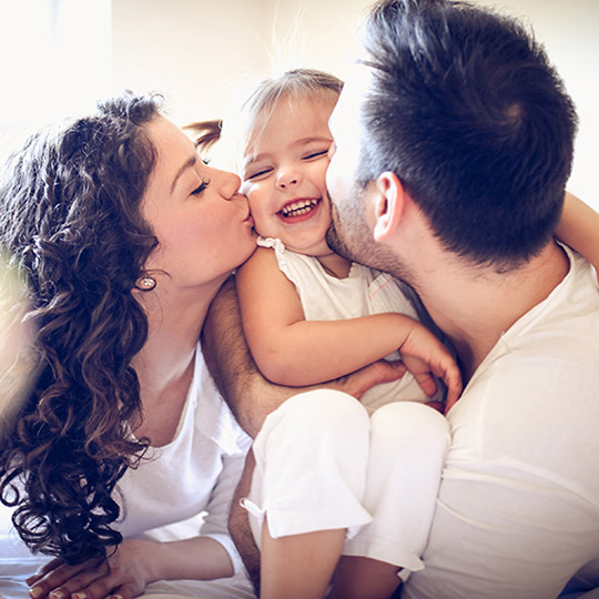 Parents both holding their little girl between them and giving her a kiss