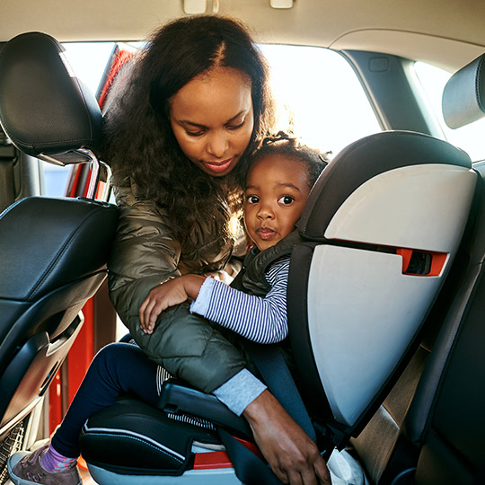 Woman buckling her youung daughter into a car seat in the back of a small car