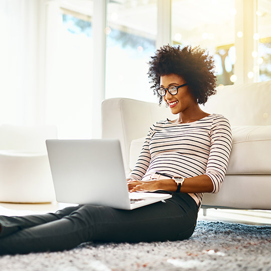 Woman sitting on her carpeted floor against the couch while working on her laptop