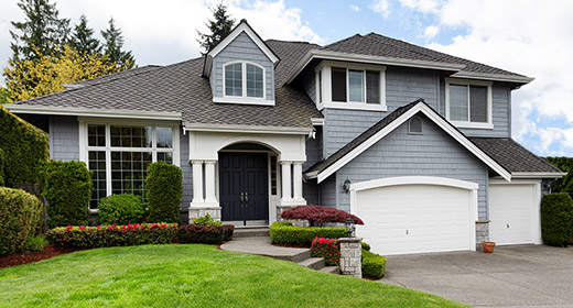Exterior shot of a house with a three car garage, gray siding, and a landscaped concrete walkway to the front door