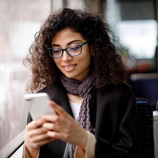 Woman looking at mobile phone while sitting on a bus near the window