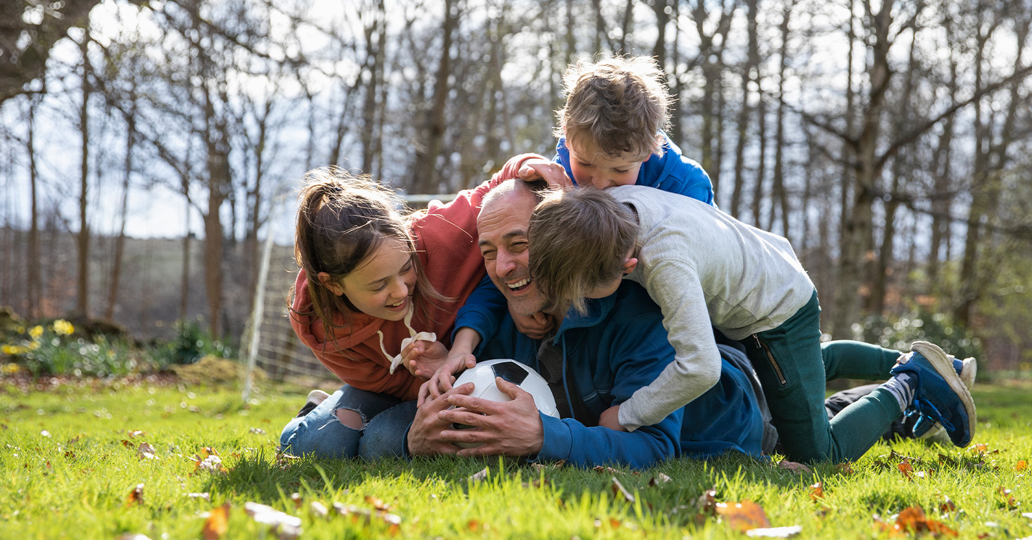 3 kids tackling their dad on a soccer field_1500x785