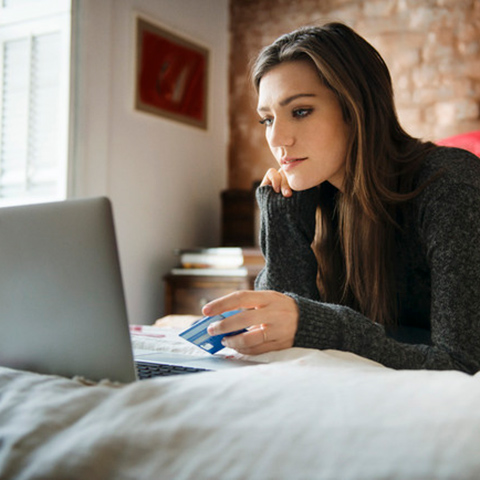 /getmedia/fa114f82 ffee 4390 ae81 101695334d5b/Girl laying on a bed preparing to type her credit card number into her laptop for an online purchase_1