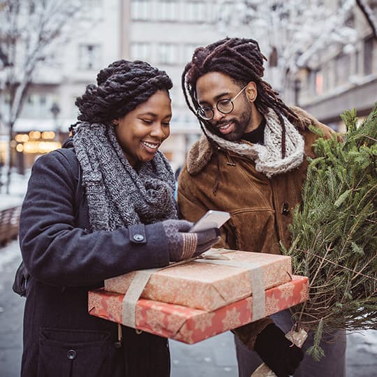 a couple walking home carrying christmas presents and a christmas tree