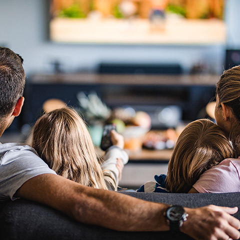 Family of two kids two parents sitting on a couch watching a movie together