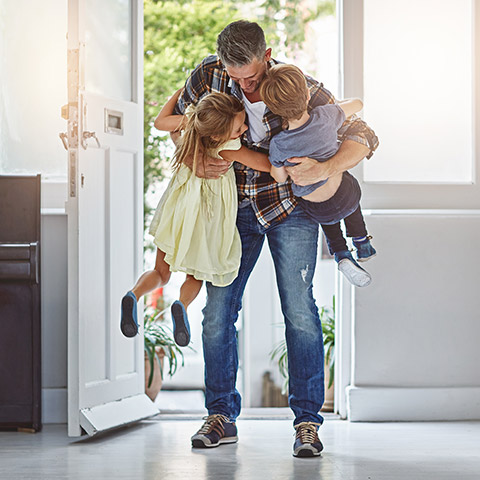 Father hugging his young son and daughter after walking in the door from a long day at work