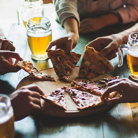 Friends sitting at a table and all reaching for a slice of pizza