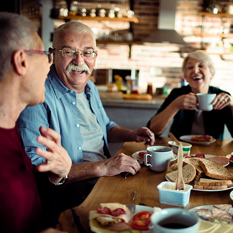 Group of older friends sitting at a kitchen table eating and laughing