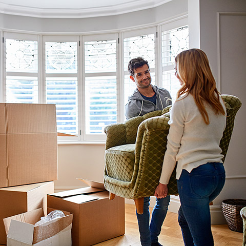 Man and woman couple carrying a couch into their new home sorrounded by moving boxes