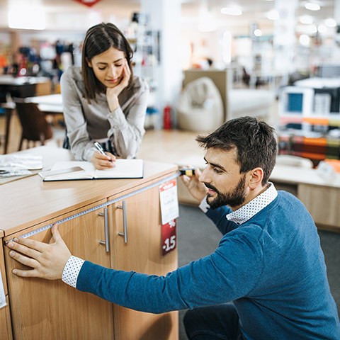 Man and woman looking at a dresser in a furniture store Man is measuring width while the woman writes down the results