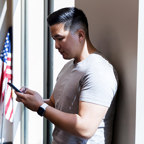 Man leaning against a wall while typing on his mobile phone