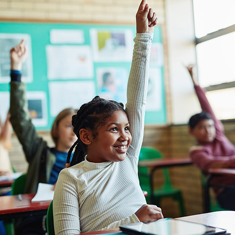 Young child in a classroom raising her hand to answer a question