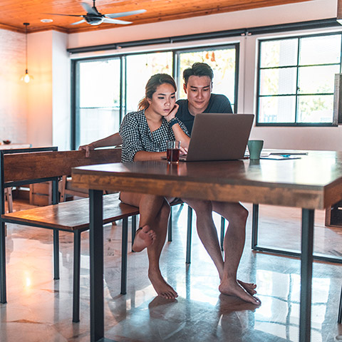 Young couple sitting at a kitchen table looking at a laptop computer