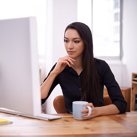 Younger woman resting her head on her hand and looking at her iMac computer